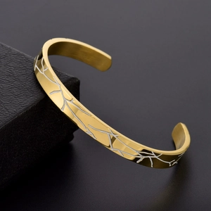 Detailed view of golden C-shaped cuff bracelet with branch etching on polished surface
