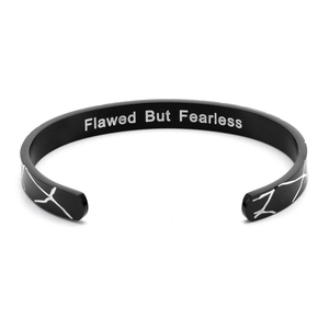 Macro shot of Flawed But Fearless engraving on black wood-patterned C-shaped steel cuff