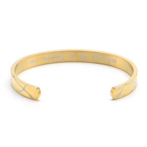 Detail of gold C-shaped cuff bracelet with silver crackle pattern and engraved quote