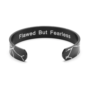 Close-up of black C-shaped cuff bracelet with white crackle pattern and engraved quote