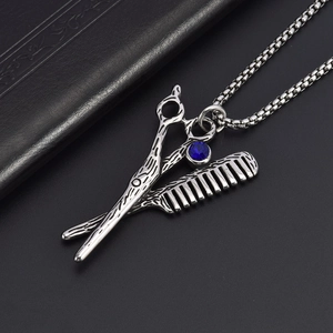 Vue détaillée du pendentif ciseaux et peigne de coiffeur avec une pierre bleue au centre