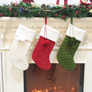 Close-up of three knitted Christmas stockings hanging by a warm fireplace with pom-poms