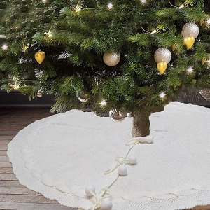 Close-up of cream white knitted Christmas tree skirt with pom poms and ribbon bows