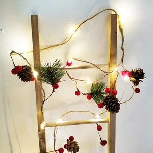 Christmas pine cone and red berry LED string light wrapped on a wooden ladder