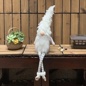 Detail of a white plush Nordic gnome with striped legs and silver shoes on a wooden bench