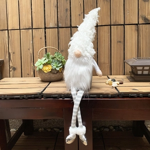 Close-up of a Christmas gnome with white fuzzy hat and striped long legs on wooden bench