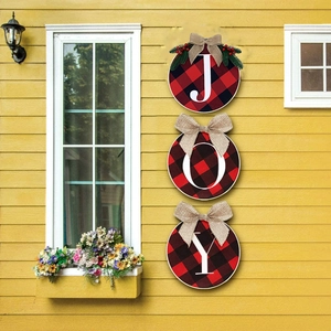 Close-up of JOY buffalo plaid round wooden signs hanging on a bright yellow exterior wall