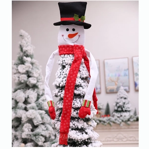 Detail view of a plush snowman tree topper with long arms wrapping around a Christmas tree