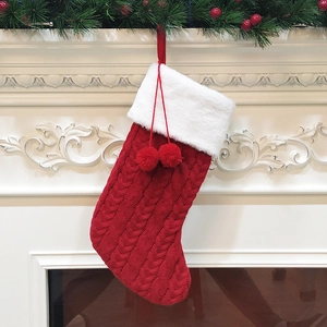 Classic red knitted Christmas stocking with white faux fur cuff and pom poms on a fireplace