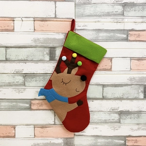 Detail of red Christmas stocking with reindeer embroidery and green cuff hanging on wall
