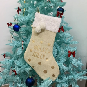 Dettaglio calza di Natale in juta con pois dorati e scritta HOLLY JOLLY su albero blu