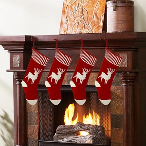 Set of four red knitted Christmas stockings with white reindeer hanging on fireplace mantel