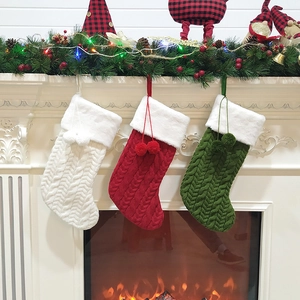 Three thickened cable knit Christmas stockings with white faux fur cuffs hanging on a fireplace