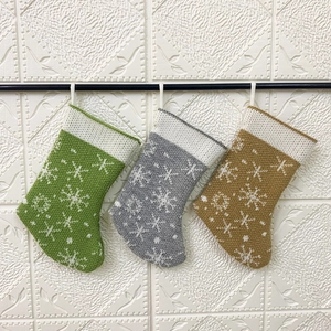 Three knitted Christmas stockings with white snowflake patterns in green, grey, and yellow