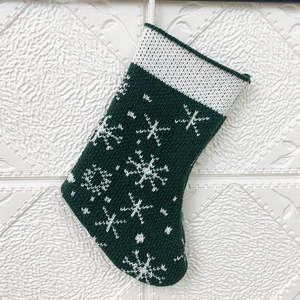 Close-up of green knitted Christmas stocking featuring white snowflake patterns and loop