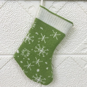 Close-up of green knitted Christmas stocking with white snowflake patterns and hanging loop