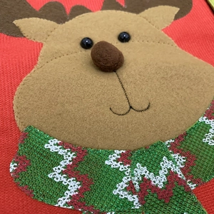 Macro detail of red knitted Christmas stocking featuring a reindeer applique with sequins