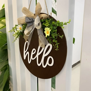 Round wooden welcome sign with hello text, burlap bow, and daisy greens hanging on a white door