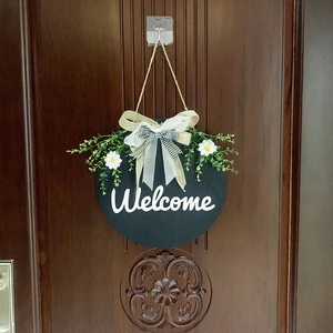 Detail of a round welcome sign with a buffalo plaid bow and artificial daisies on a door
