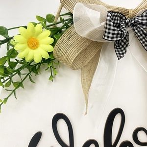 Detail of yellow daisies, burlap bow, and black 3D Hello text on wooden sign