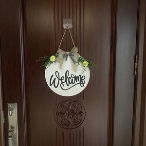 Detail of wooden welcome sign with burlap bow, greenery and daisies on dark wood door