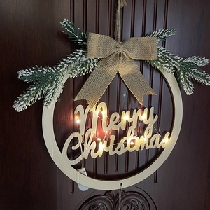 Illuminated wooden Christmas wreath with Merry Christmas carving and burlap bow on a door