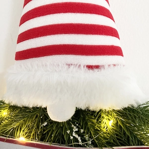 Close-up of Christmas gnome wreath with striped knit hat, pine needles and LED lights