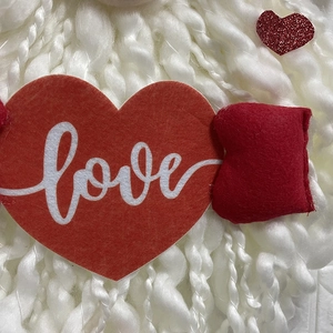 Detail of plush Valentine gnome with red felt heart featuring love text and glitters