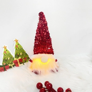 Makroaufnahme eines Weihnachtszwergs mit roten Pailletten und warmem Licht auf Kunstfell