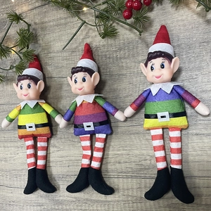 Three Christmas male elf dolls in rainbow outfits with pine needles on wood background