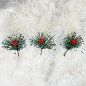 Three artificial Christmas pine needles with red berries on a soft white faux fur background