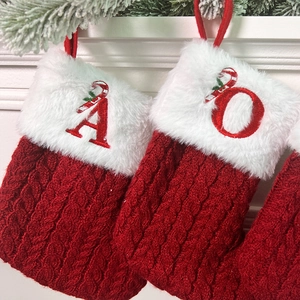 Close-up of red cable knit Christmas stockings with plush white trim and embroidered letters
