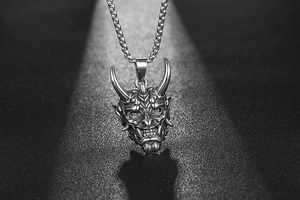 Gros plan du pendentif masque Hannya argenté avec chaîne carrée sur texture noire