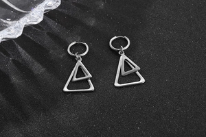 Gros plan de boucles d'oreilles triangles en acier inoxydable sur fond noir moderne