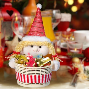 Christmas elf plush doll holding a striped gift basket on a warm festive table