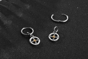 Macro detail of men's stainless steel hoop earrings with gold nautical pendant