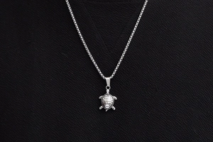 Detailed top view of a realistic stainless steel sea turtle pendant on a pearl chain