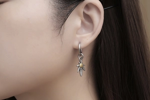 Macro detail of silver feather earring with gold emblem in vintage Japanese style