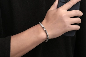 Macro close-up of men's braided silver chain bracelet with intricate wheat link texture