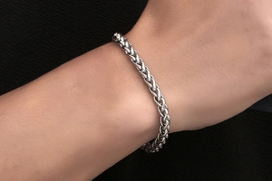 Close-up of a masculine silver wheat chain bracelet worn on a wrist with textured background