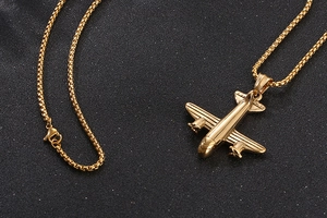 Gros plan d'un pendentif avion doré poli avec une chaîne box sur une texture noire