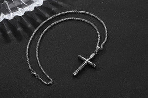 Close-up of vintage gun-grey titanium cross pendant with textured industrial grid pattern