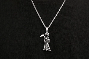 Macro shot of gothic Santa Muerte reaper pendant with scythe and owl on dark background