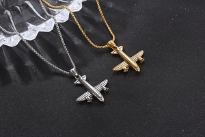 Détail de pendentifs avion en or et argent avec chaînes à mailles carrées sur fond noir