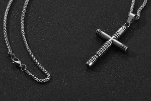 Macro shot of vintage titanium steel cross pendant with dotted texture and woven chain
