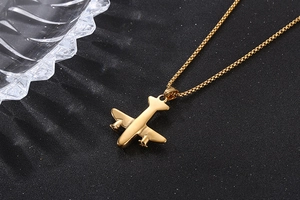 Détail d'un collier pendentif avion doré sur un fond noir texturé élégant