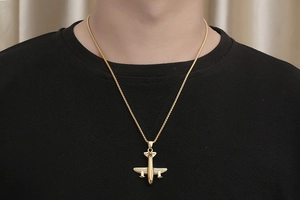 Vue détaillée du collier pendentif avion en or poli porté par un mannequin sur noir