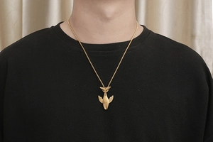 Detail eines goldenen Walflossen-Anhängers an einer feinen Kette auf schwarzem Shirt