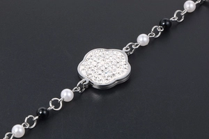 Détail macro d'un charm fleur argenté avec zircons, perles blanches et perles noires