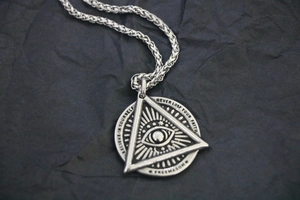 Detailed close-up of vintage steel Freemason eye pendant on textured black background